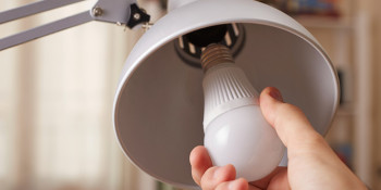 Image of a hand changing a regular light bulb for LED